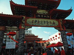 People in Los Angeles Chinatown stroll under red lanterns as they enter a Chinese building on a beautiful day with a clear blue sky.