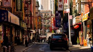 In Chinatown, New York, Chinese shops are gazed at by people while cars park alongside buildings.