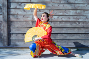 A beautiful woman wearing a traditional Chinese costume holds two big yellow fans—Chinatown in Rome concept.